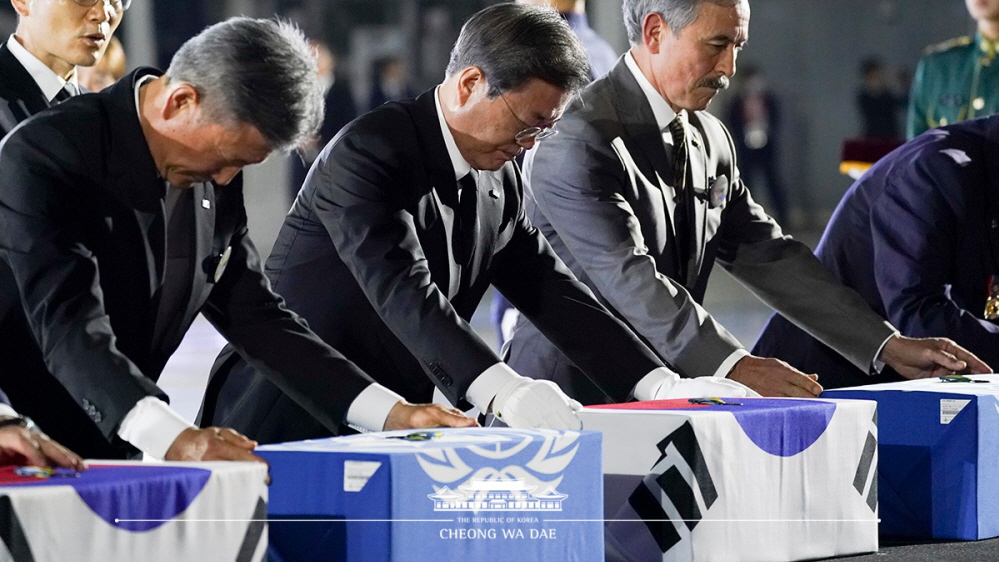 President Moon Jae-in (left) on June 25 attends at Seoul Air Base an event commemorating the 70th anniversary of the Korean War's outbreak, placing badges of service on the remains of fallen soldiers and paying a silent tribute.